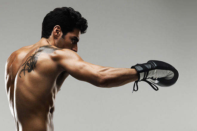 Tattooed muscular male fighter punching in the air against plain background