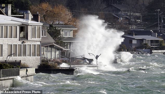 Waves crash against a seawall next to homes at high tide during a windstorm Thursday